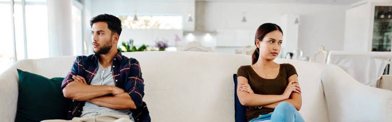 couple sitting on a couch, arms folded, facing away from each other.