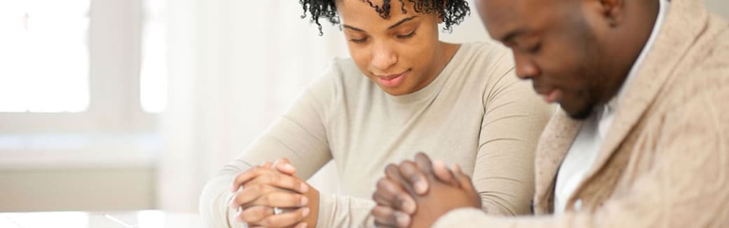 husband and wife sitting at a table together praying