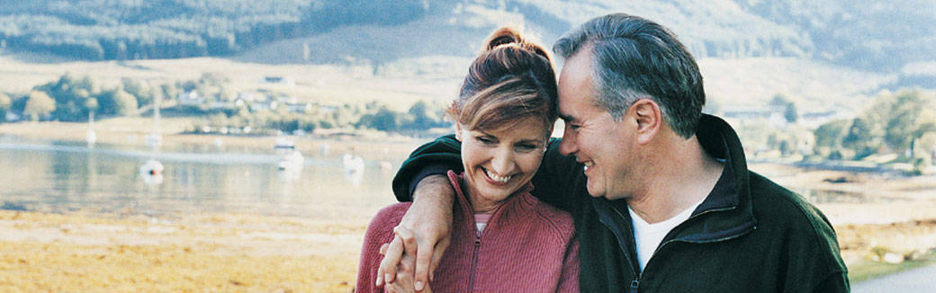 older couple outside, smiling, with heads together