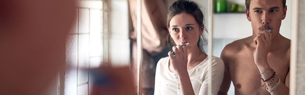 man and woman looking in a mirror brushing their teeth